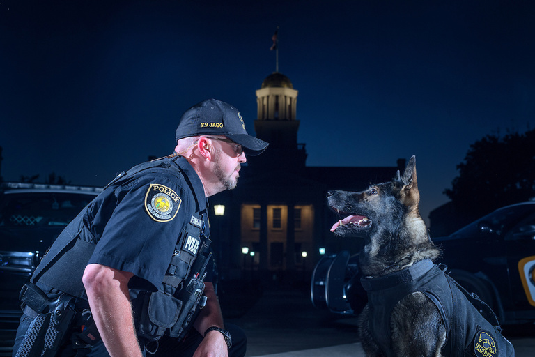 Officer Bernhard and K9 Jago pose in front of the Old Capitol at dusk.